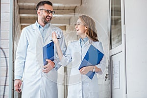 smiling vets in white coats walking with clipboards in veterinary clinic and looking at each other