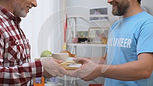 Smiling volunteer bringing breakfast to old man in nursing home care and support