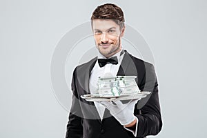 Smiling waiter in tuxedo and gloves holding tray with money