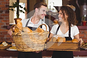 Smiling waiter and waitress holding basket full of bread rolls