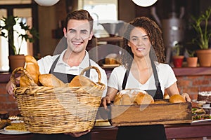 Smiling waiter and waitress holding basket full of bread rolls