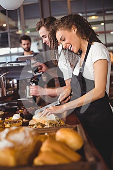 Smiling waitress cutting bread in front of colleague