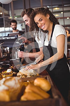 Smiling waitress cutting bread in front of colleague