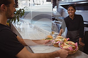 Smiling waitress giving baskets with food to coworker in cafe