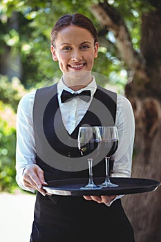 Smiling waitress holding a tray with glasses of red wine