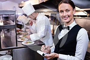 Smiling waitress with note pad in commercial kitchen