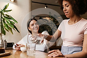 Smiling waitress pouring water in glass while serving for woman in cafe