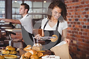 Smiling waitress putting bread roll in paper bag