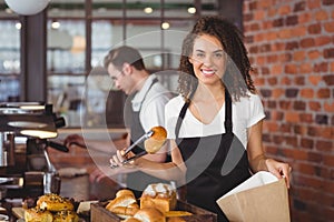 Smiling waitress putting bread roll in paper bag