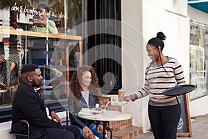 Smiling waitress serving two young friends at a sidewalk cafe