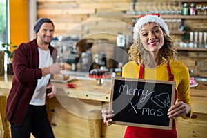 Smiling waitress standing with merry x mas sign board in cafe