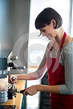 Smiling waitress using a tamper to press ground coffee into a portafilter