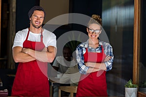 Smiling waitress and waiter standing with arms crossed outside cafÃÂ©