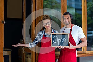 Smiling waitress and waiter standing with open sign board outside cafÃÂ©