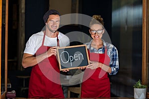 Smiling waitress and waiter standing with open sign board outside cafÃÂ©