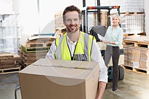 Smiling warehouse worker carrying box