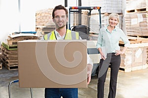 Smiling warehouse worker carrying box