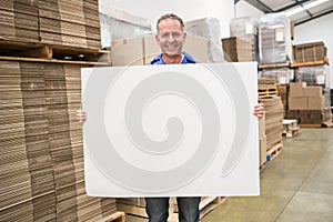 Smiling warehouse worker holding large white poster