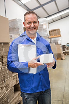 Smiling warehouse worker holding small box and clipboard