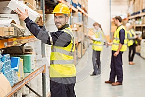 Smiling warehouse worker taking package in the shelf