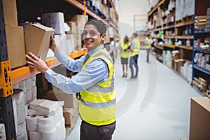 Smiling warehouse worker taking package in the shelf