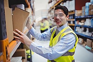 Smiling warehouse worker taking package in the shelf