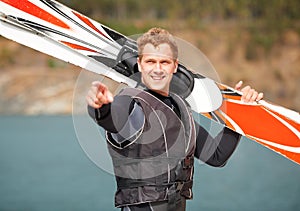 Look at that guy there. Smiling water-skier holding his skis alongside the lake and pointing.