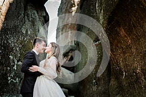 Smiling wedding couple stands hugging between the rocks