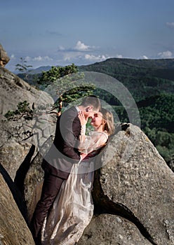 Smiling wedding couple stands hugging between the rocks