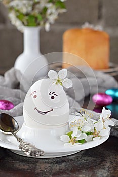 Smiling white egg and flowers on clay plate. Happy Easter card. Holidays breakfast concept. Festive table place setting decoration