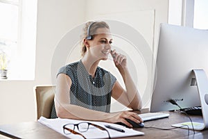 Smiling white woman at computer in an office wearing headset