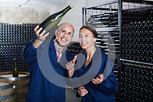 Smiling winery workers holding bottle of wine