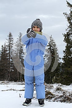Smiling winter child with ski outfit playing with cold snow