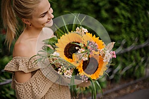 Smiling woman accurate holds bouquet with sunflowers in her hands.
