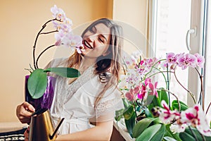 Smiling woman admires blooming purple orchid holding pot. Girl gardener taking care of home plants and flowers.