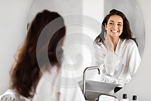 Smiling woman admiring herself in bathroom mirror photo