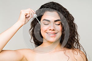 Smiling woman applying hyaluronic acid oil to her face