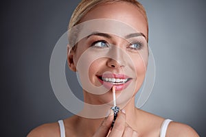 Smiling woman applying lip-gloss on lips