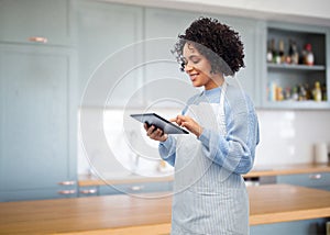 smiling woman in apron with tablet pc in kitchen