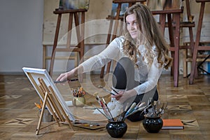 Smiling woman artist sits on the floor in art studio and paints