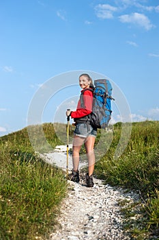 Smiling woman with backpack and trekking poles on the mountain t