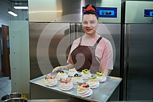 Smiling woman baker presenting tray with set of meringue nests