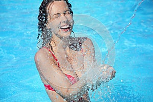 Smiling woman bathes in pool under water splashes photo