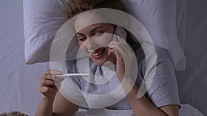 Smiling woman in bed holding pregnancy test and talking phone, positive result