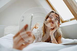 Smiling woman on bed, taking selfie with phone in comfort