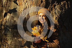 Smiling woman in beige coat and orange hat against huge tree