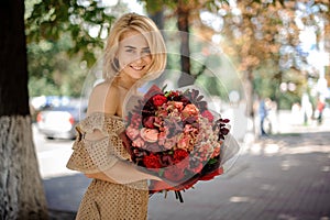 Smiling woman in beige dress holds in her hand bouquet of bright red flowers.