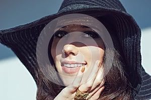 Smiling woman in black raffia hat. Gold openwork jewelry.