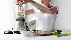 Smiling woman with blender and green vegetables
