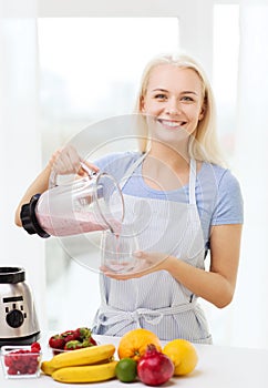 Smiling woman with blender preparing shake at home